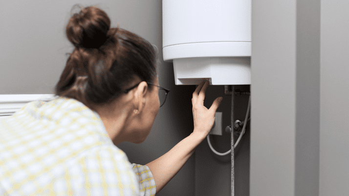 A woman wearing glasses adjusts a water heater.