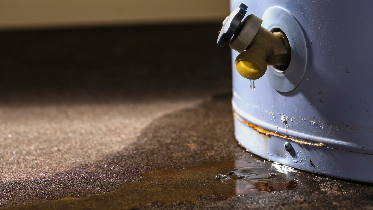 An old water heater leaks, leaving a rusty puddle below it.